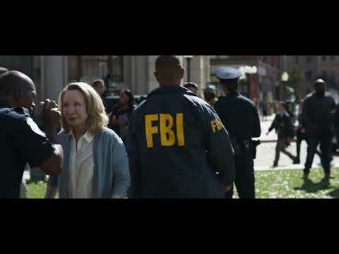 A man in an FBI jacket walks through a crowd.