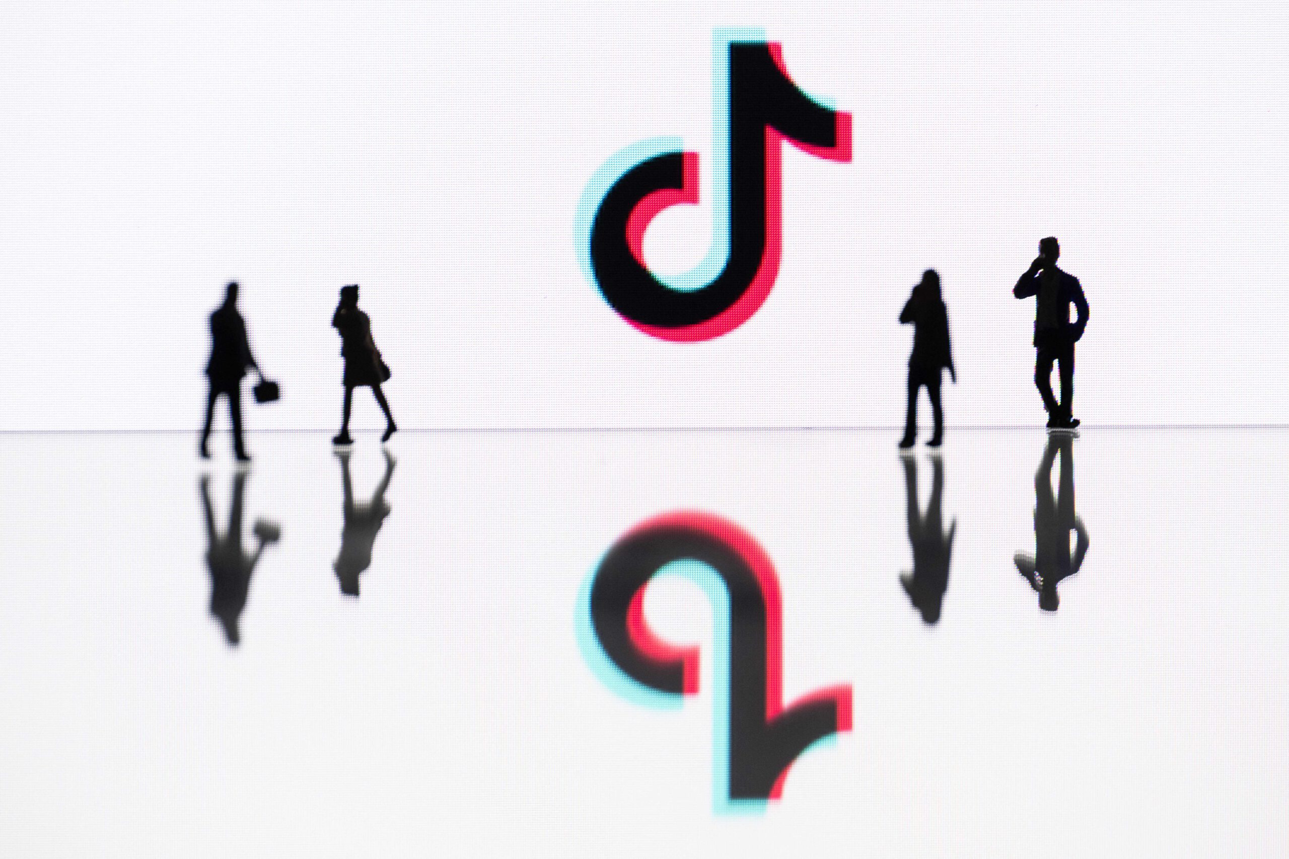The TikTok logo framed by the shadows of four people. 