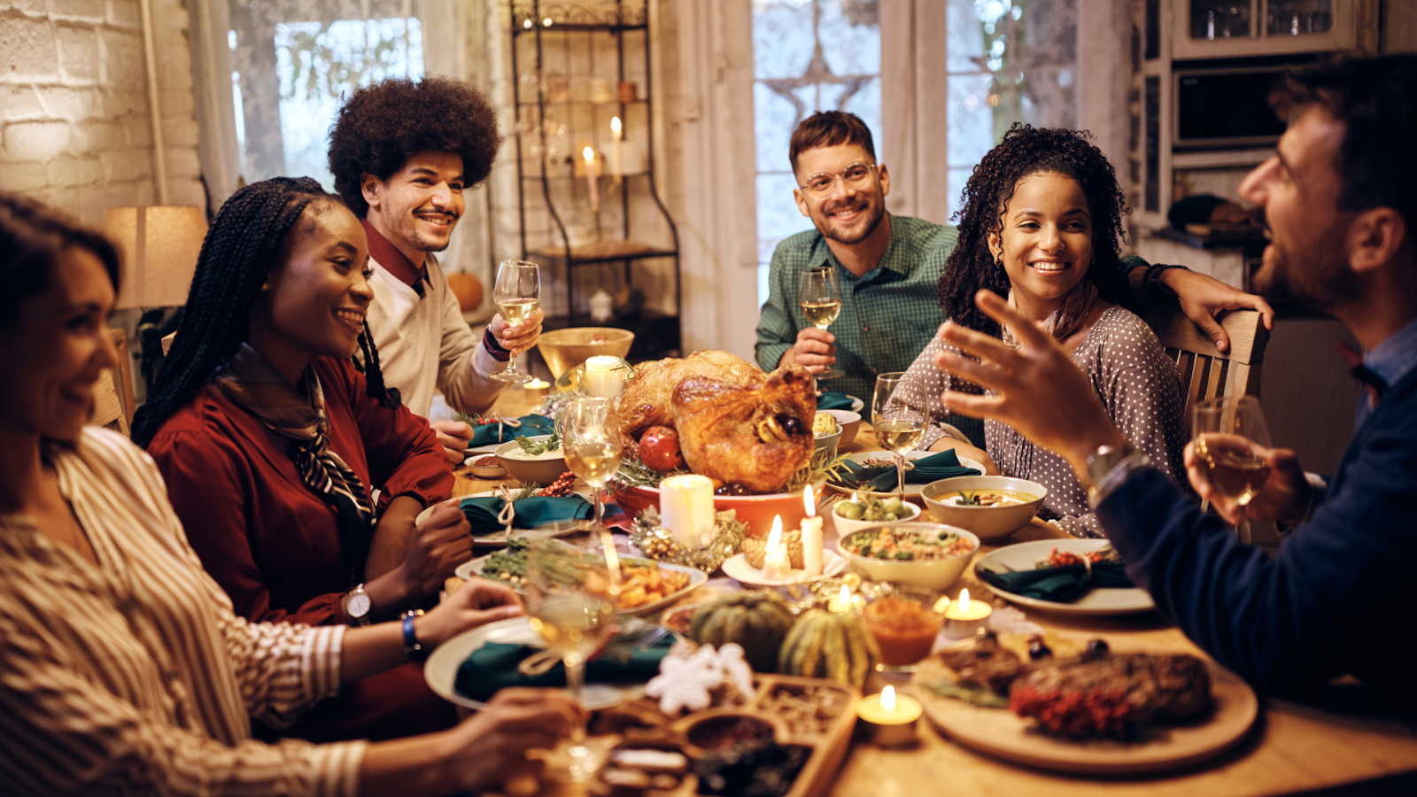 Young happy friends talking at dining table during Thanksgiving lunch