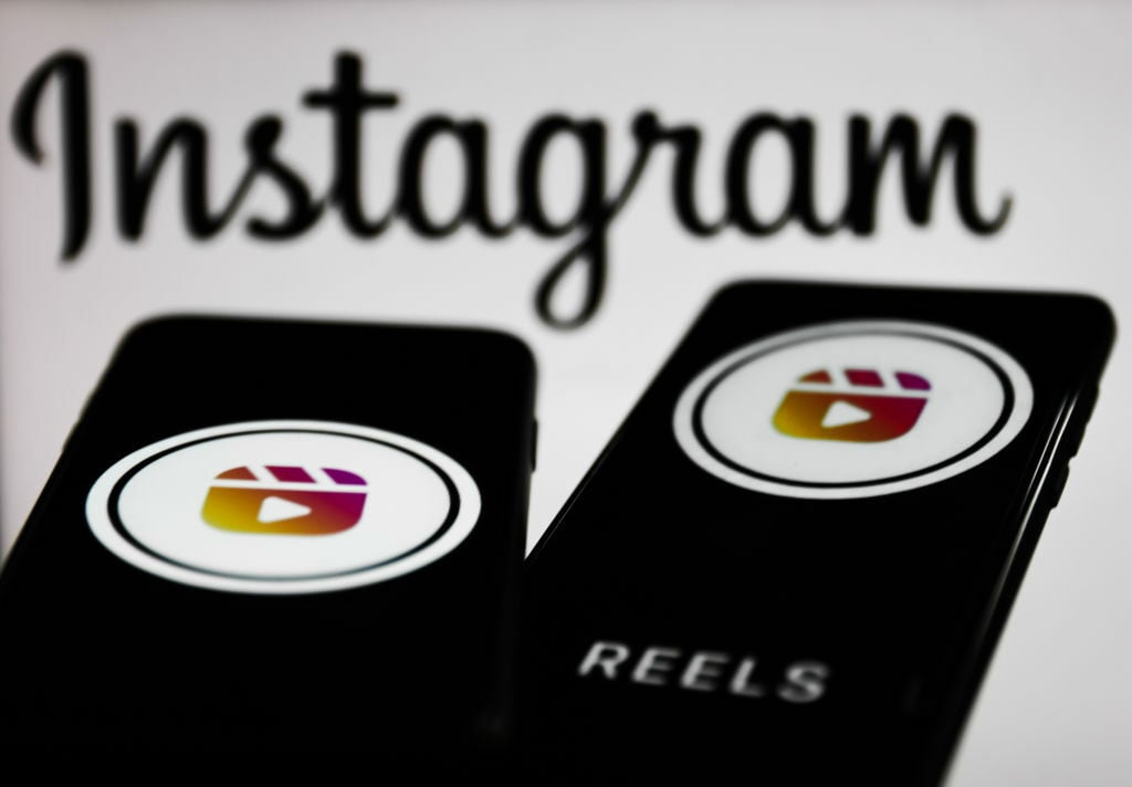 Instagram Reels logos displayed on a phone screens and Instagram logo displayed on a screen in the background.