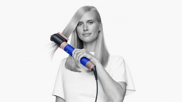 a person with long blonde hair uses the dyson airwrap hair dryer 