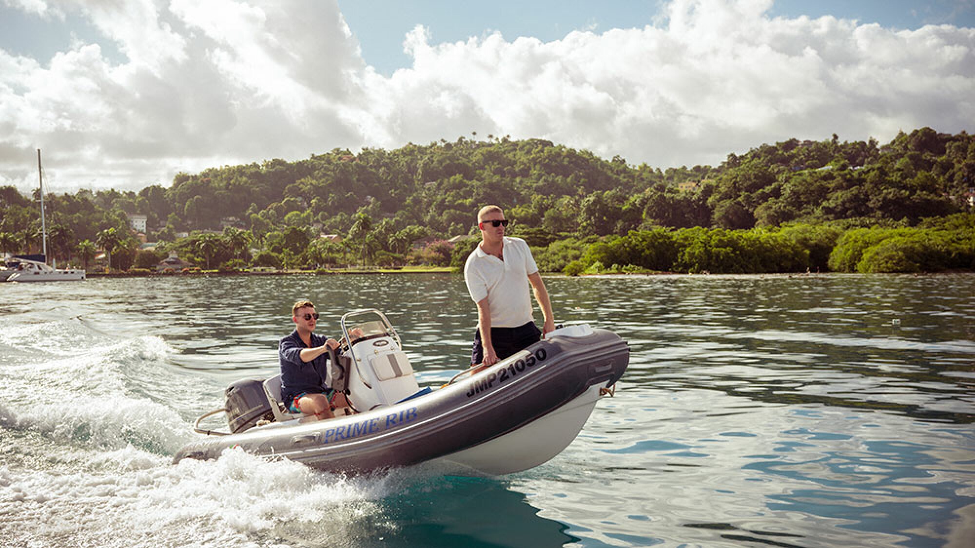 Two men in sunglasses stand on a motorboat in a sunny location.