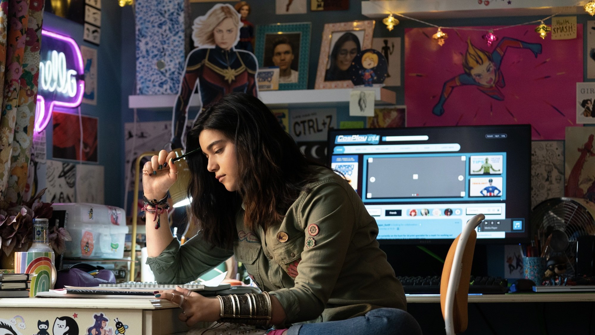 Kamala Khan from "The Marvels" drawing at her desk in her room, surrounded by posters of Captain Marvel.