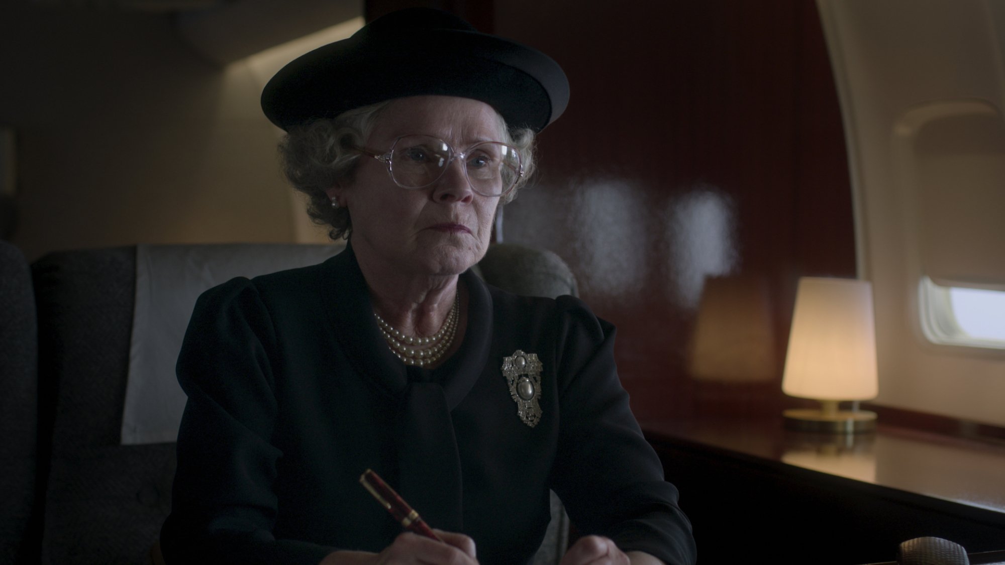Imelda Staunton as Queen Elizabeth II sitting in a plane in black.