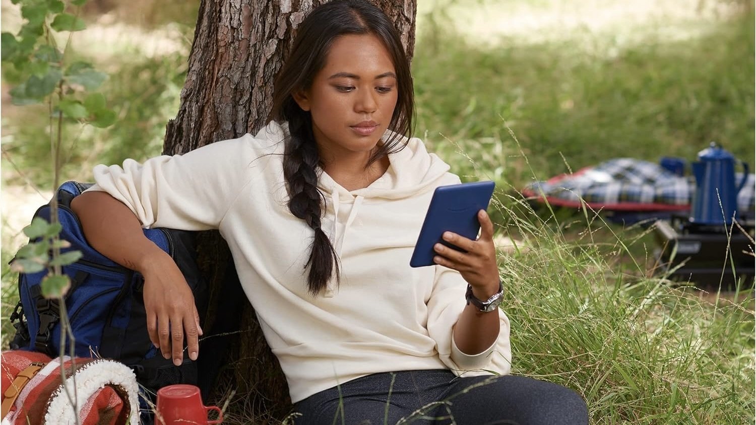 person reads on kindle sitting against trees outdoors