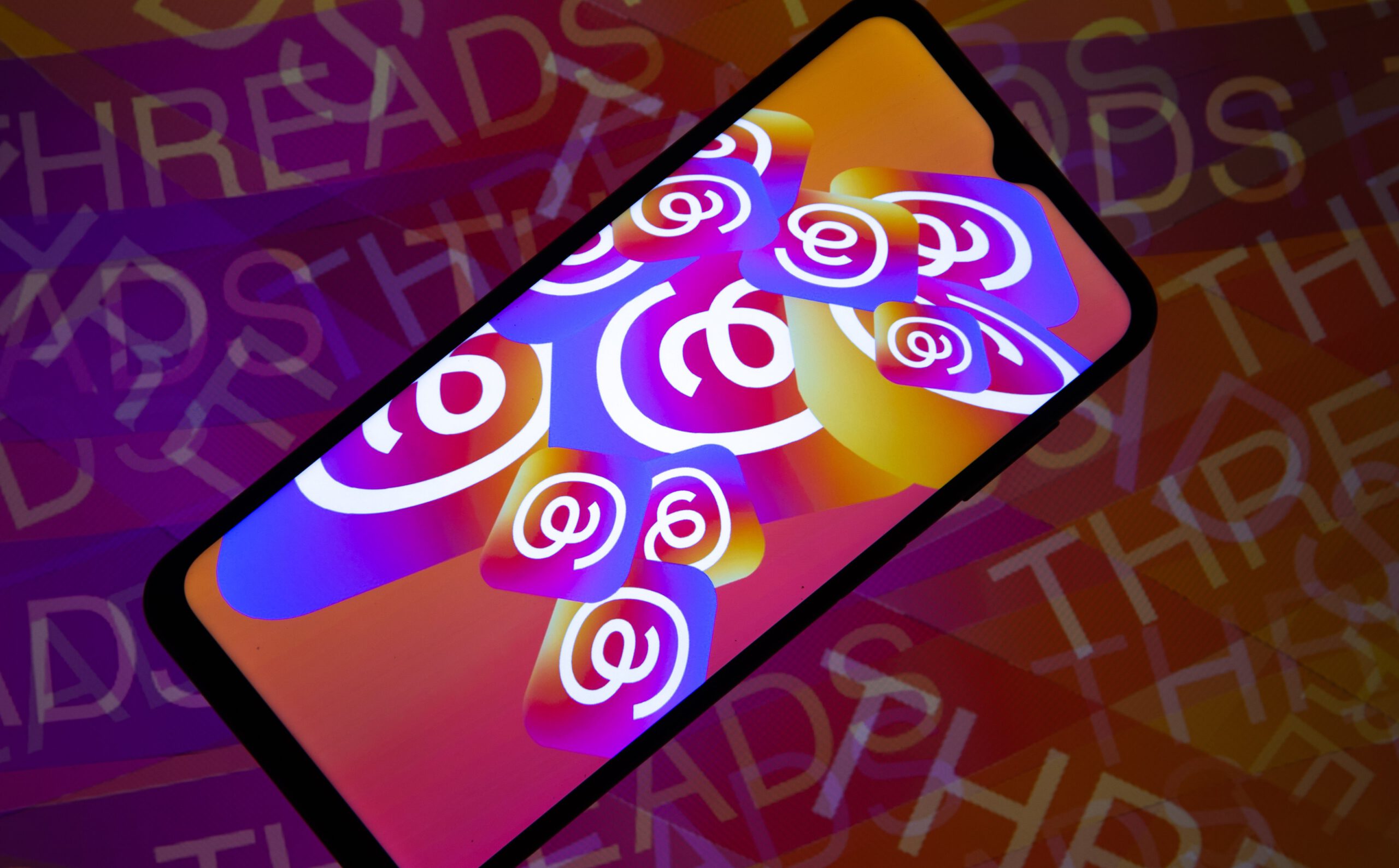A phone screen displaying overlapping rainbow threads logos on a faded background reading, 
