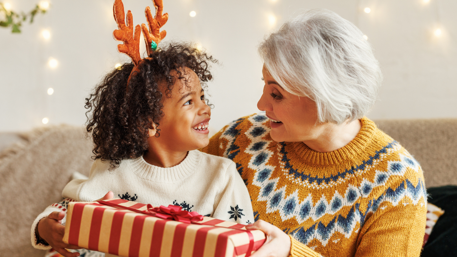Happy afro american curly boy sitting on grandmother lap with christmas present, smiling at camera