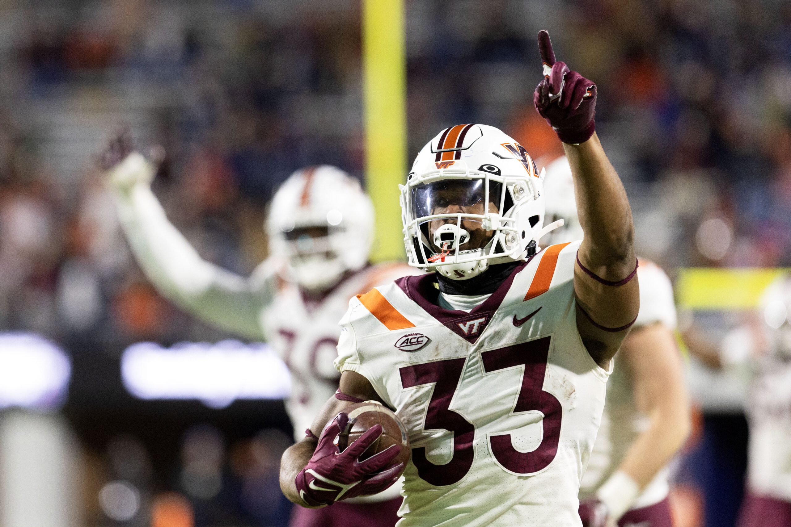 Virginia Tech player holds a football and points in the air.