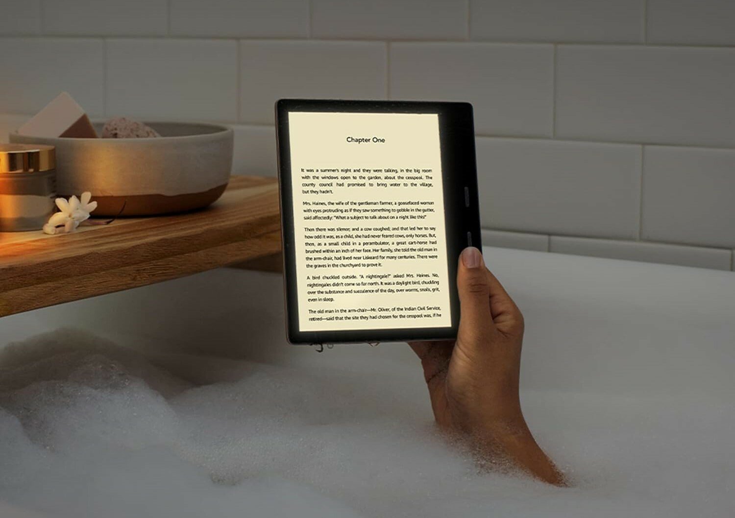 a right hand holds a kindle e-reader in a bathtub full of soapy water