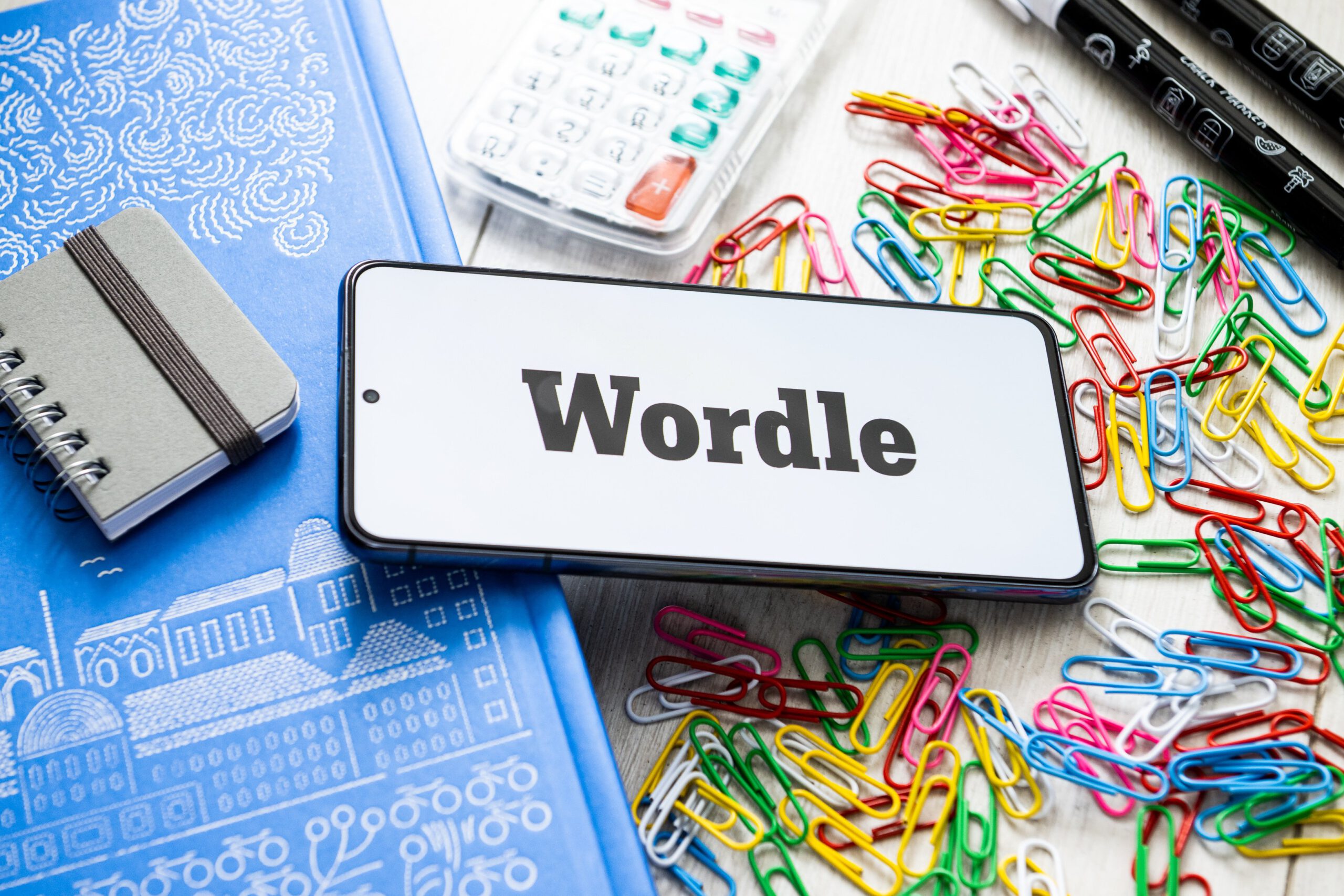 A Wordle logo seen displayed on a smartphone against a cluttered desk.