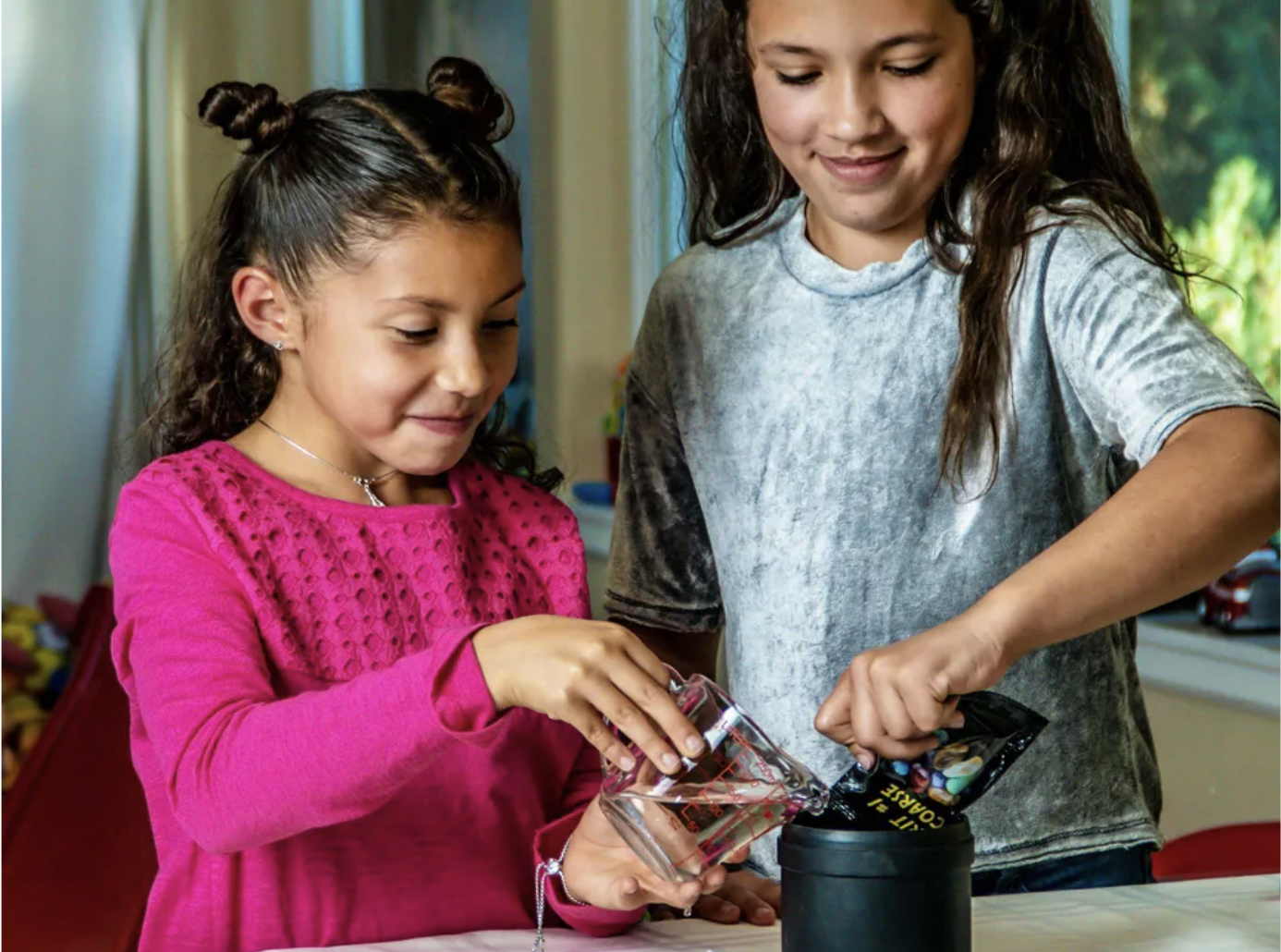 Two girls holding component parts of the Nat Geo Rock Tumbler kit while following the kit's instructions