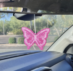 A hot pink butterfly-shaped freshener coming hanging on a car's rearview mirror.