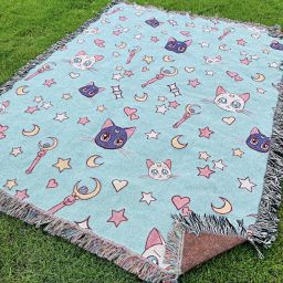 The blanket laid out on a grass field. It's is blue, with Artemis (white), Luna (purple), plus the Moon Stick and white pink and yellow stars, moons, and hearts.