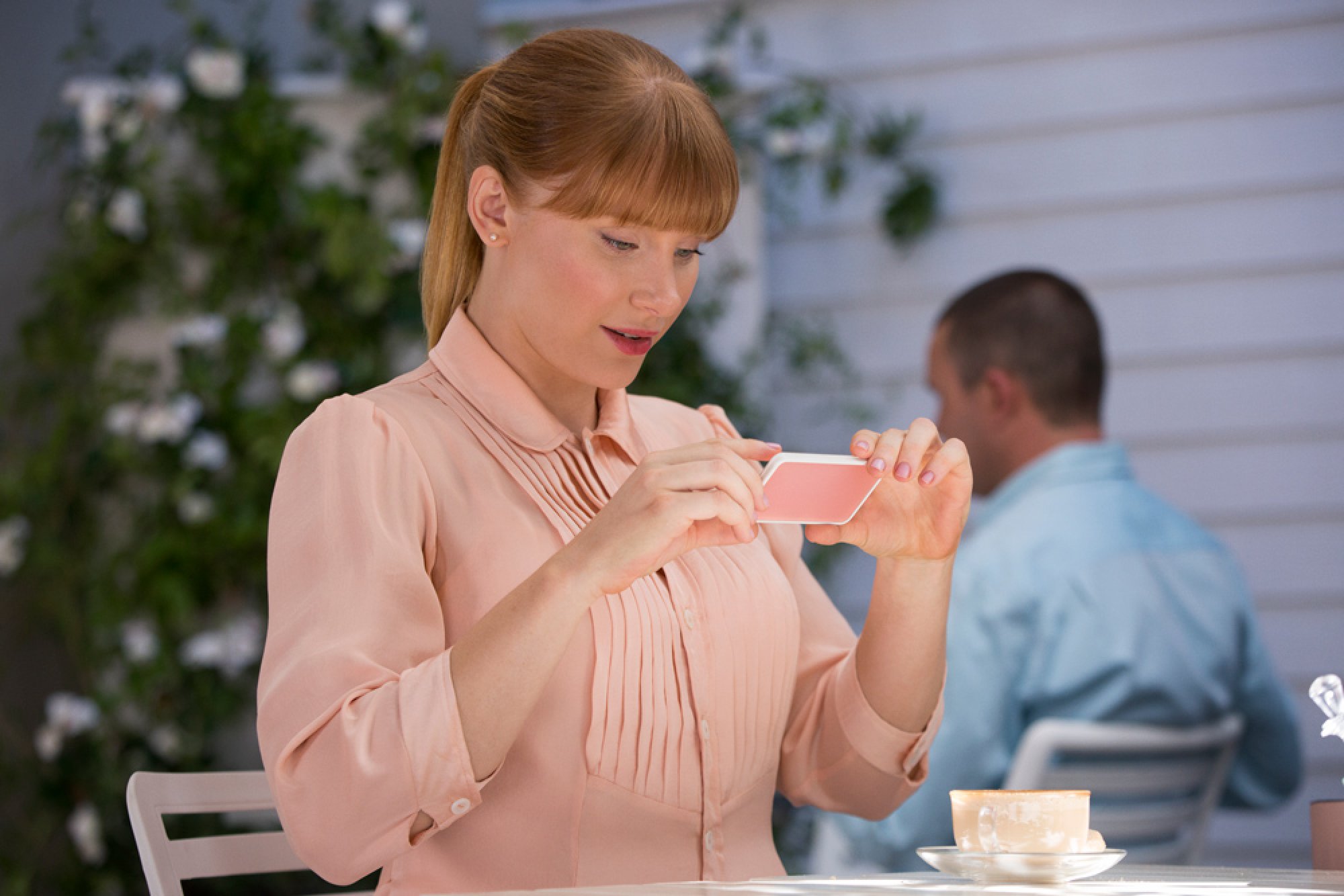 Bryce Dallas Howard as Lacie in "Black Mirror" episode "Nosedive." She is taking a photograph of her drink at a cafe.