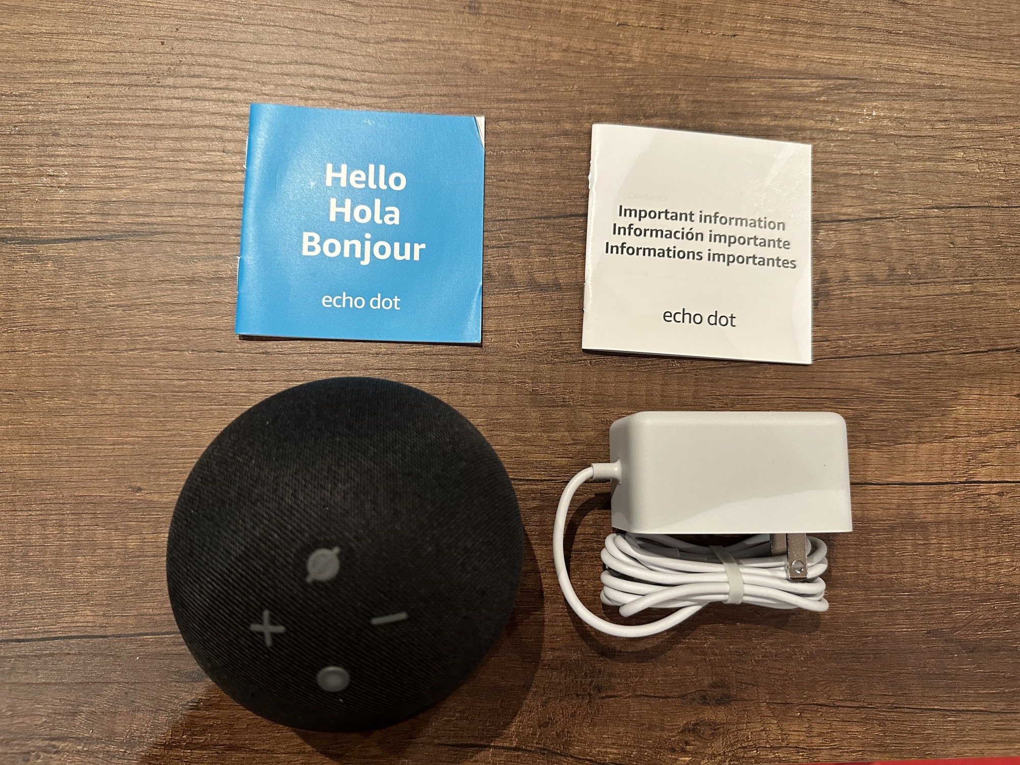 The Amazon Echo Dot resting on a table alongside its cord and two instruction manuals for use