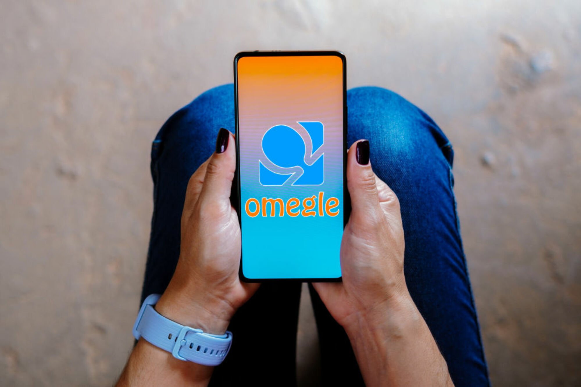 the omegle logo on a smartphone being held in a woman's lap