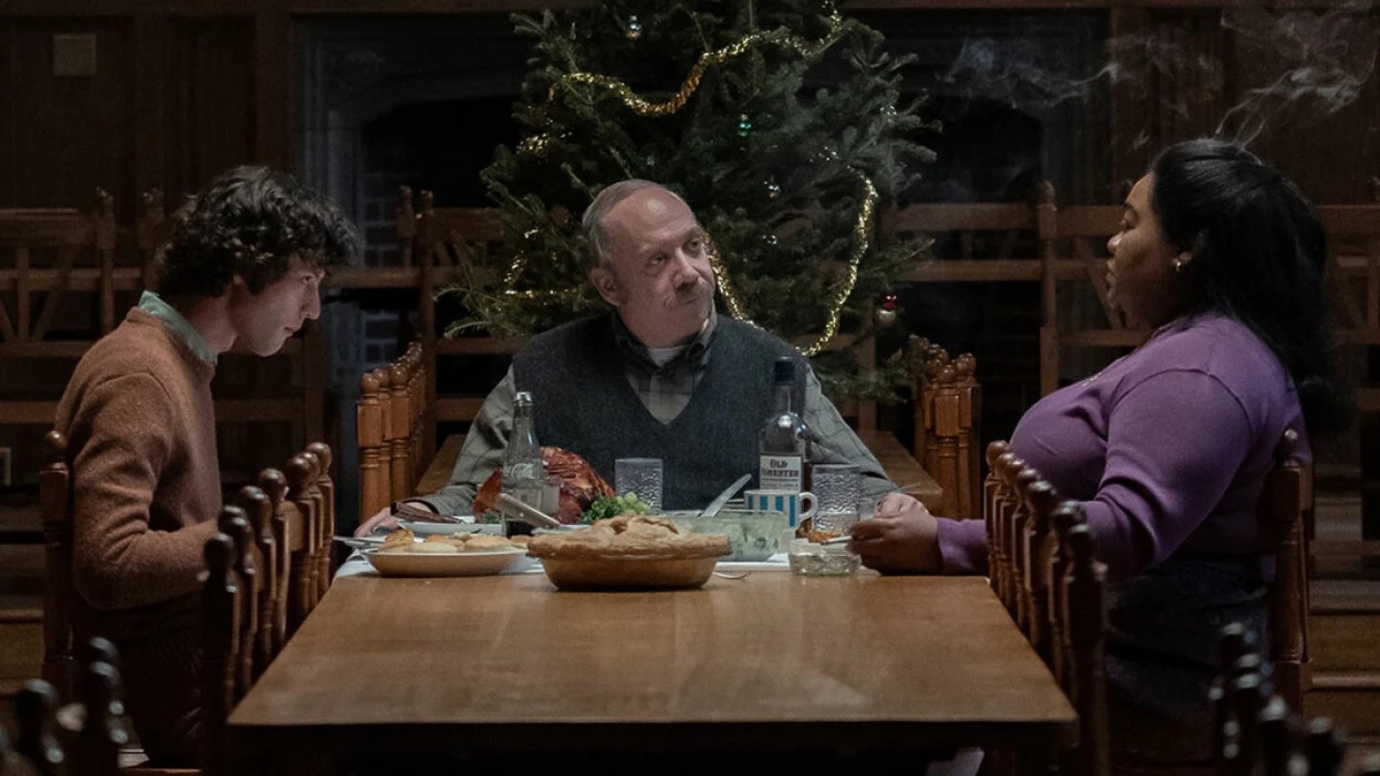 Three people eat dinner at a long table in front of a Christmas tree.