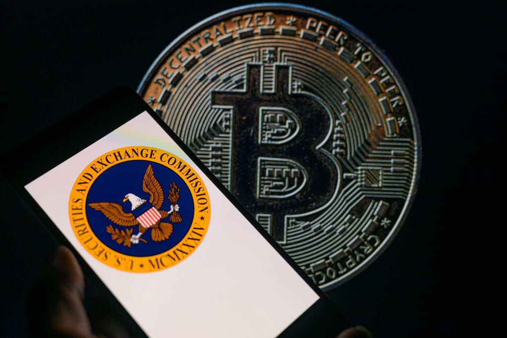 The seal of the U.S. Securities and Exchange Commission is being displayed on a smartphone, with Bitcoin visible on the screen in the background.