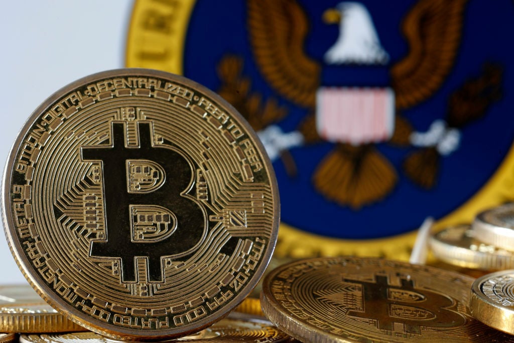 , A visual representation of the digital cryptocurrency Bitcoin is displayed in front of Securities and Exchange Commission (SEC) logo.