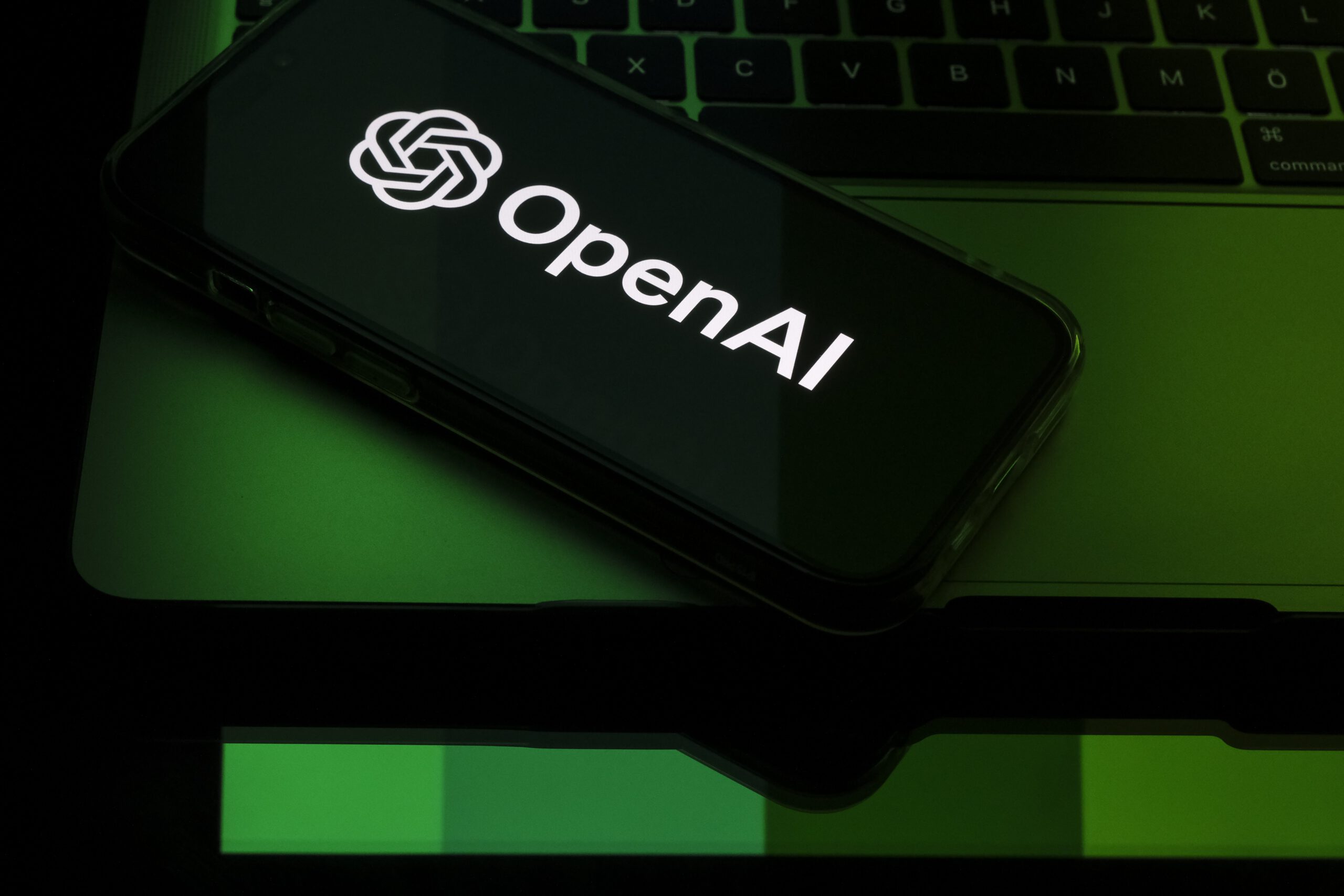A phone displays the OpenAI logo bathed in green light. 