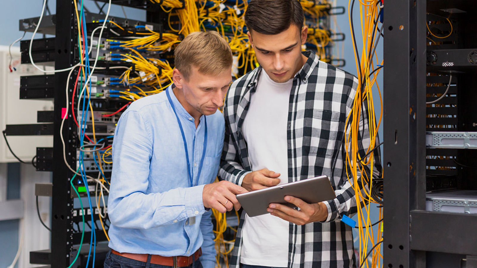 two men looking at tablet screen next to complex wiring