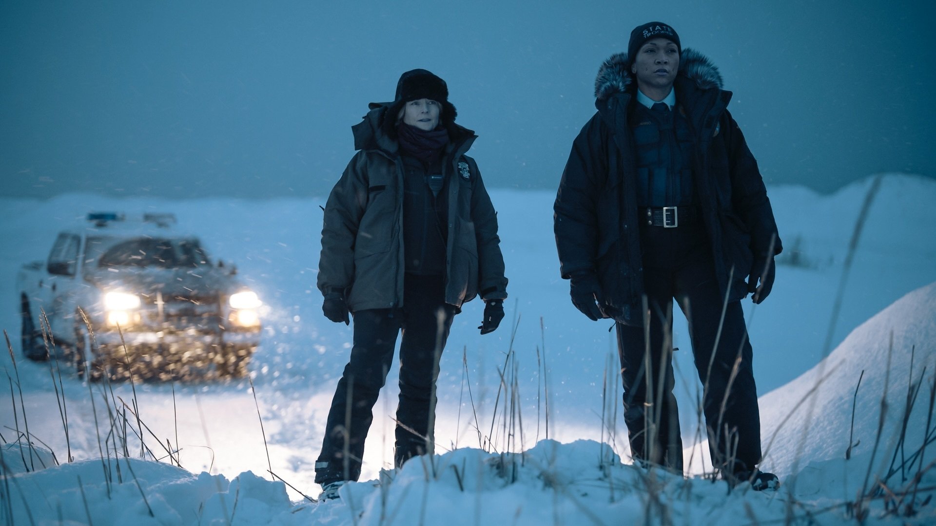 Two women in bulky coats and police uniforms stand in the snow.
