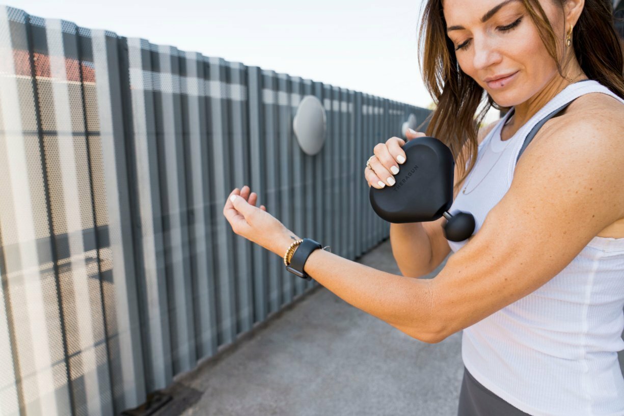 a woman uses a theragun mini on her left bicep