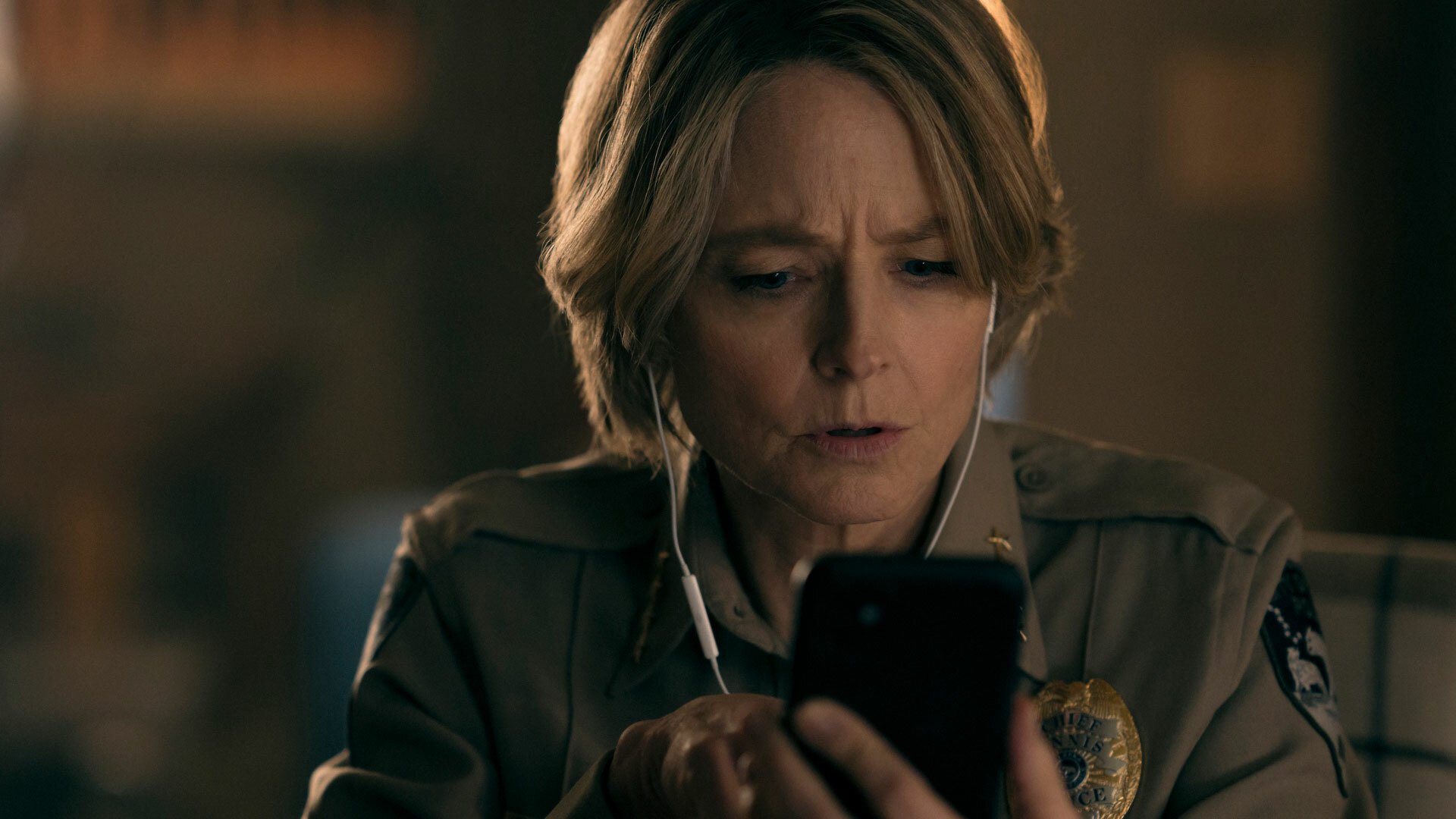 A police officer wearing headphones stares at a smartphone with concentration.