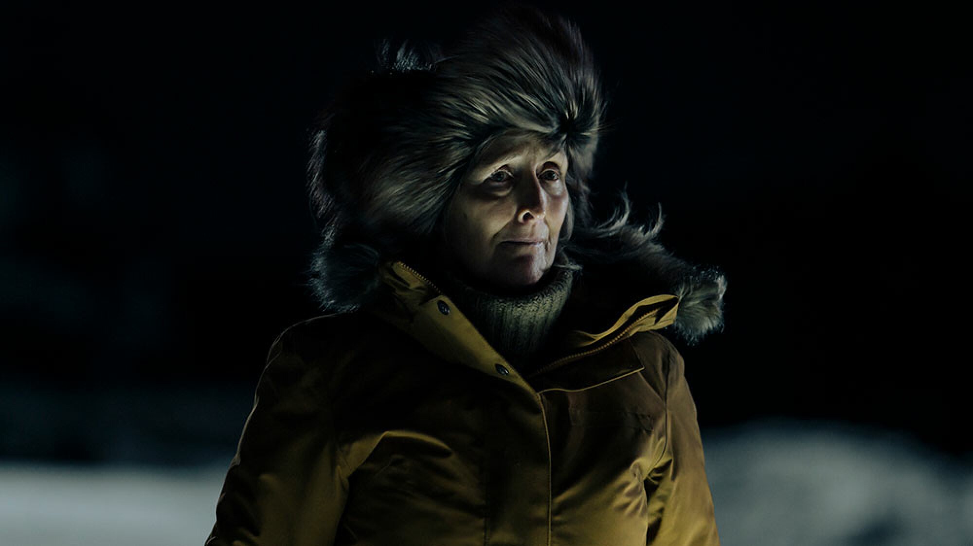 A woman stands in a coat outside in the snowy darkness.