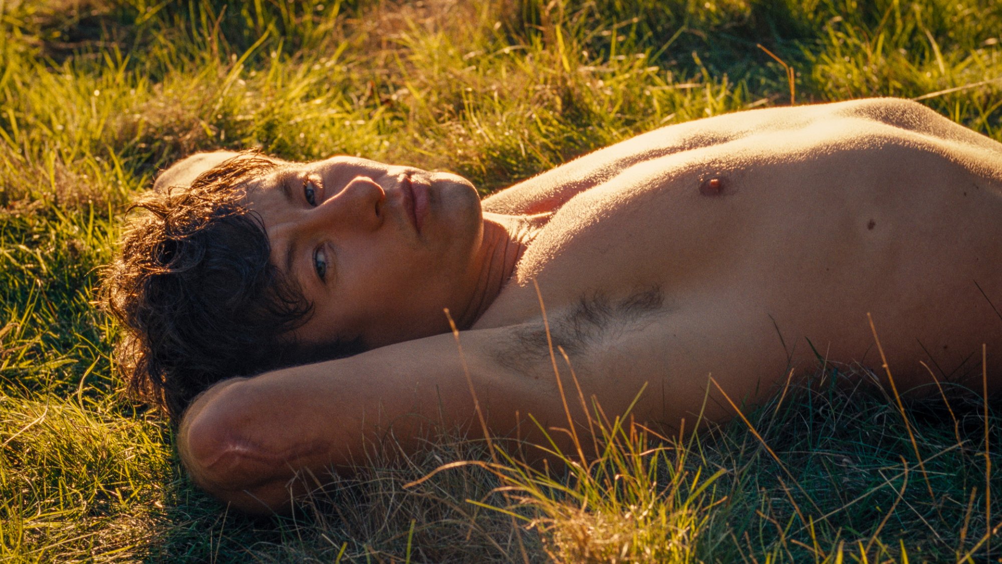 A young man lies on the grass without a shirt.