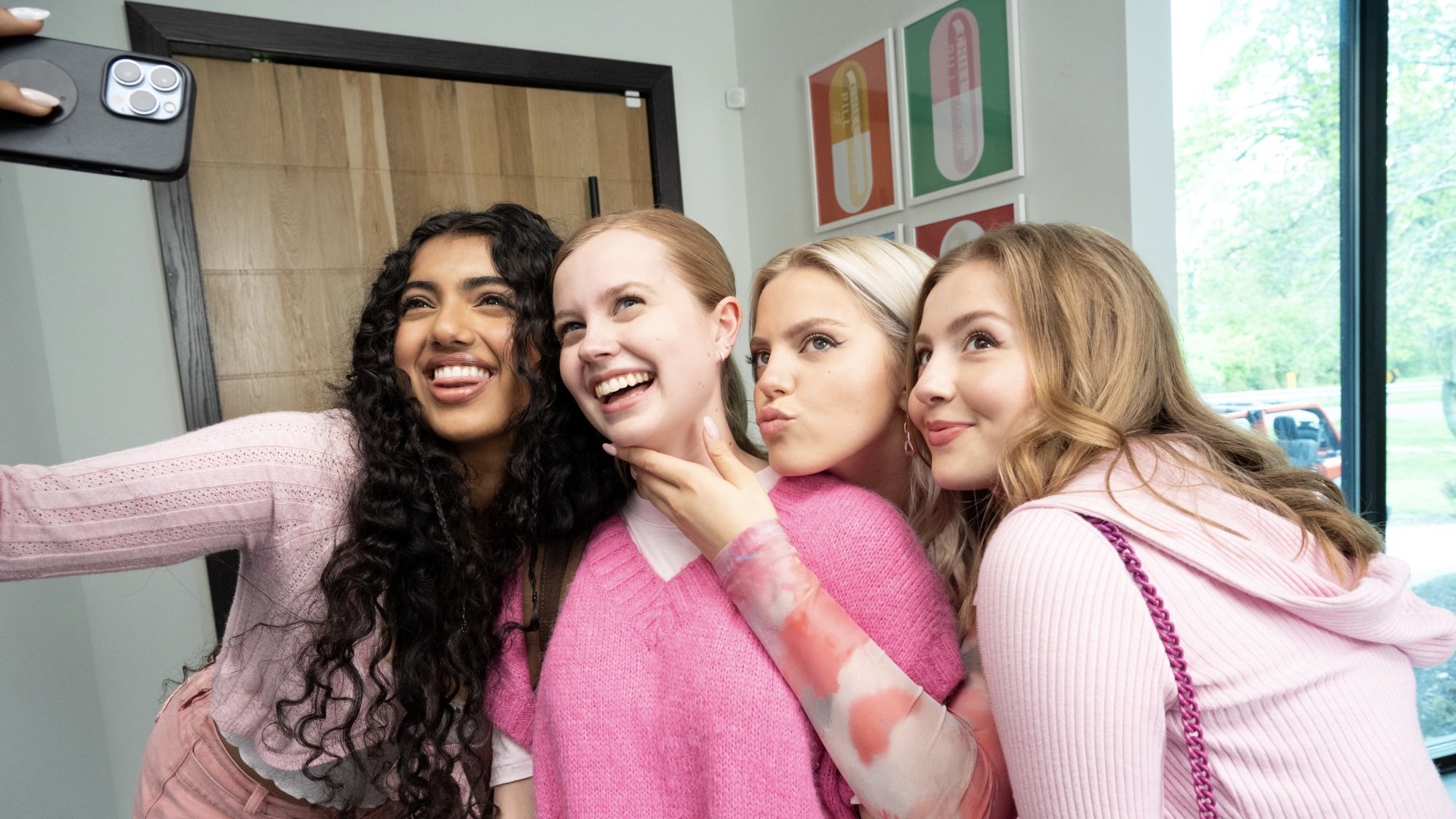 Four high school girls in pink outfits pose for a selfie.