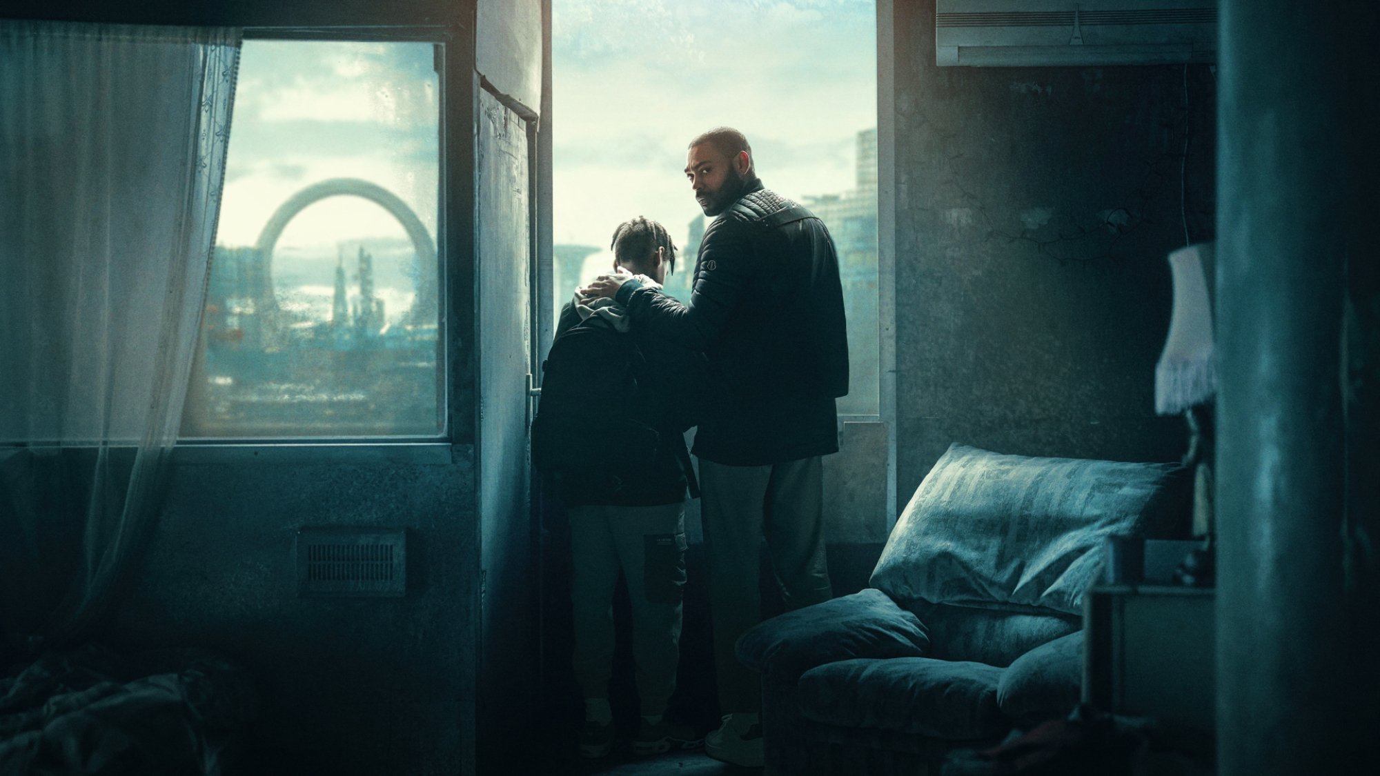A man and a boy stand at a window in a dark apartment in London.