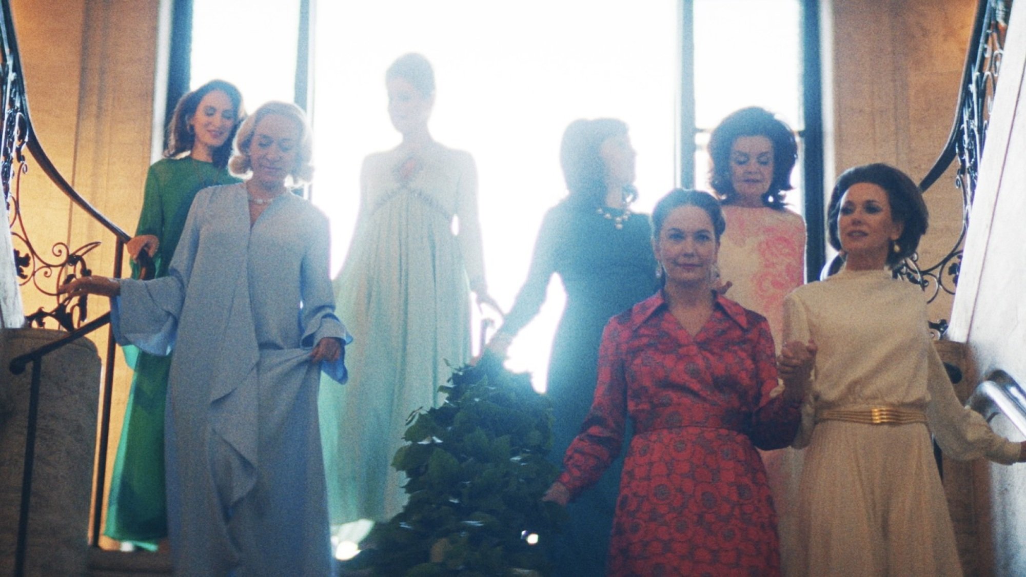 A group of women in fancy dresses walk down a large staircase.
