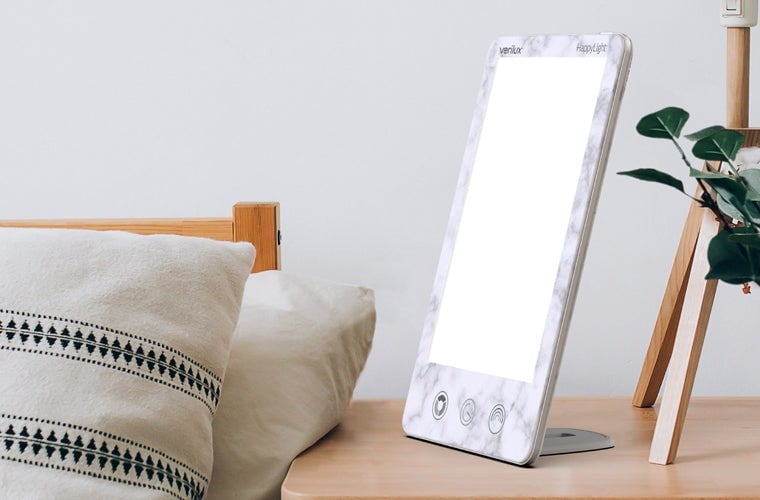 a verilux happylight luxe sits on a bedside table