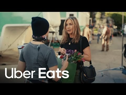 A young woman handing Jennifer Aniston a bag full of flowers.