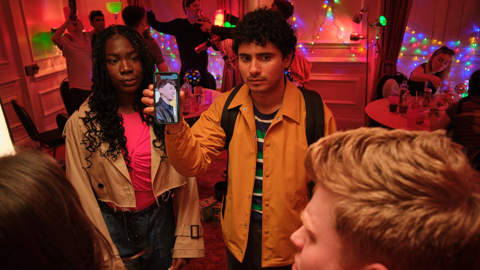 A young woman and a young man hold up a phone solemly at a party.