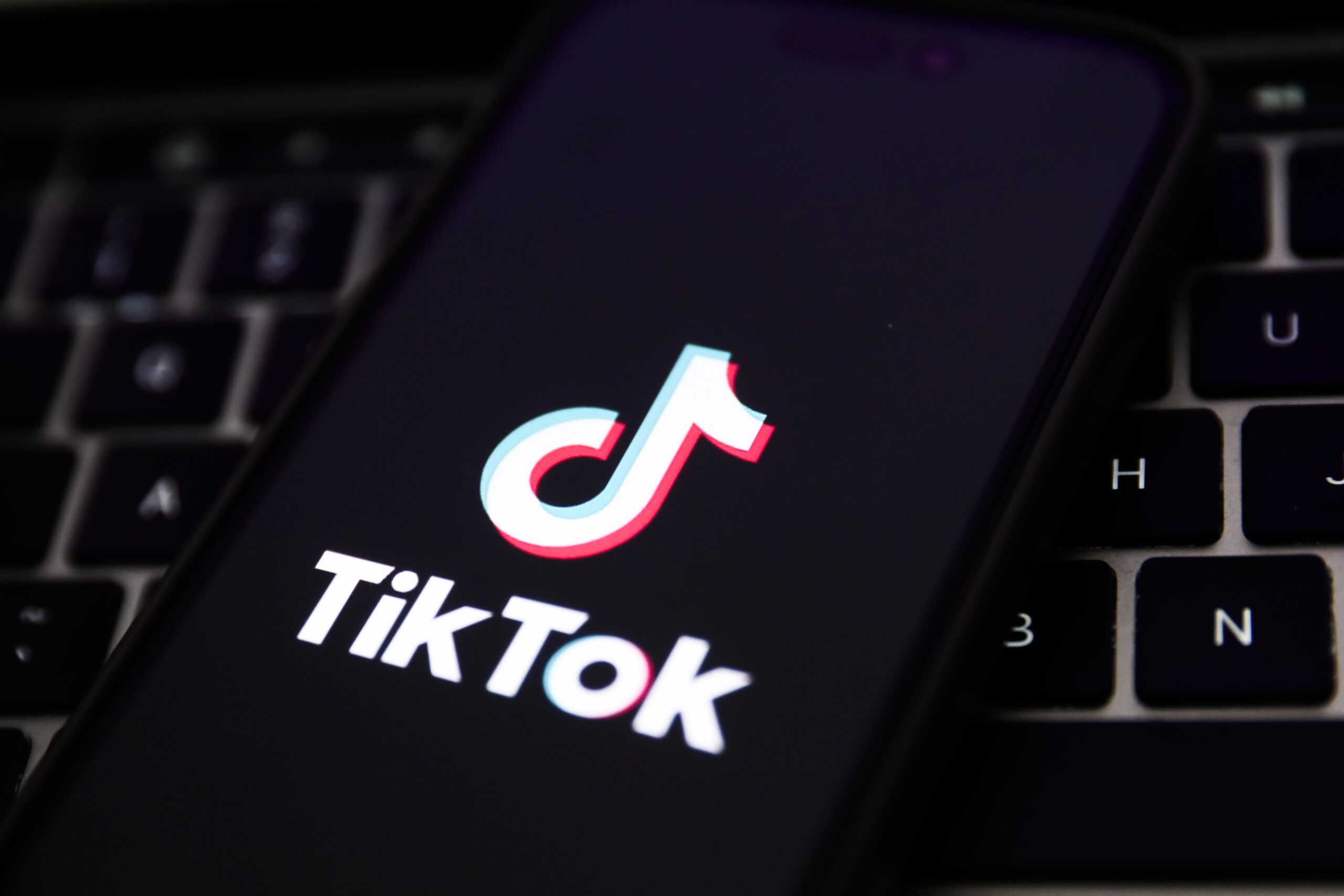 A laptop keyboard and TikTok logo displayed on a phone screen are seen in this illustration photo