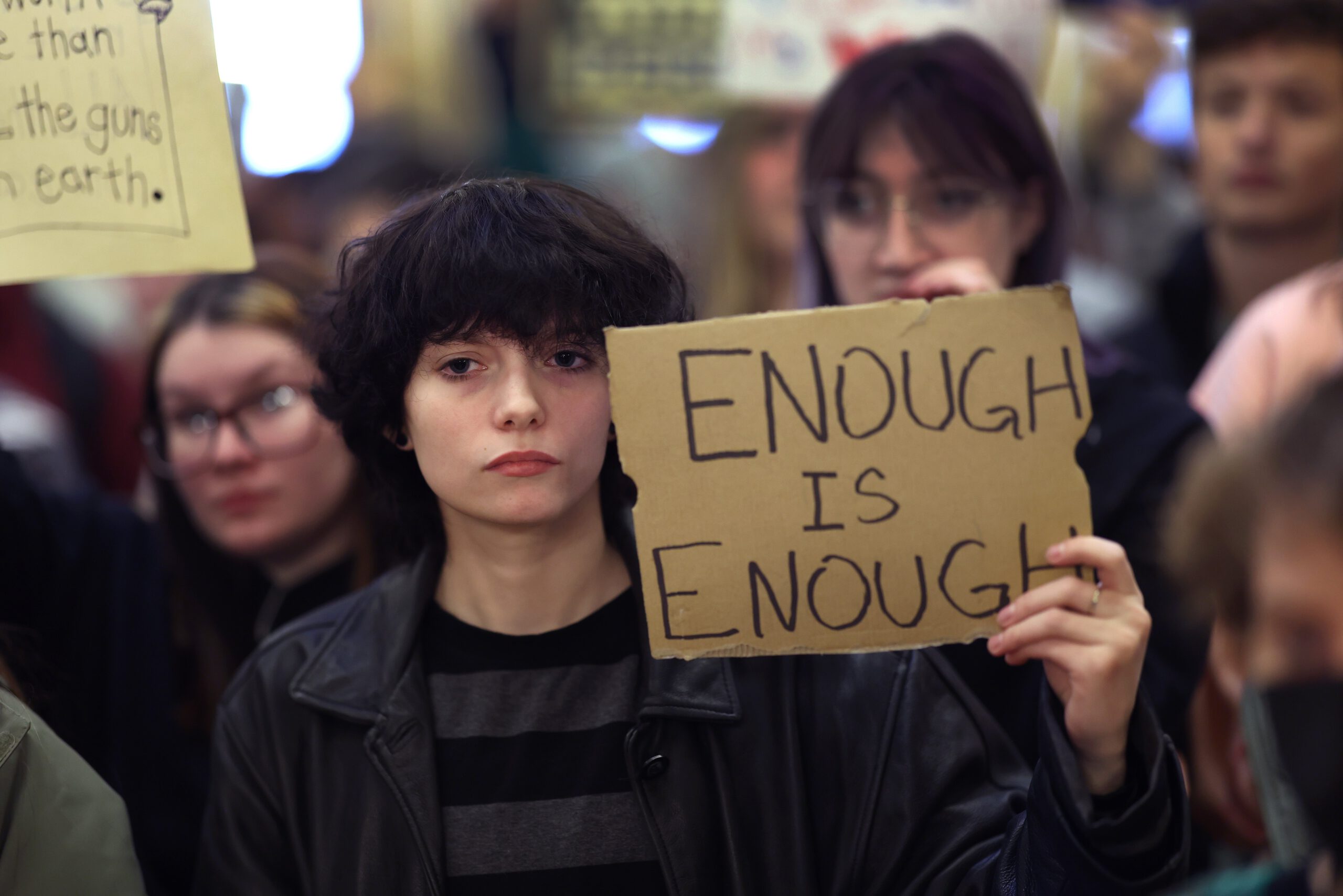 A young person holds up a cardboard sign that reads 