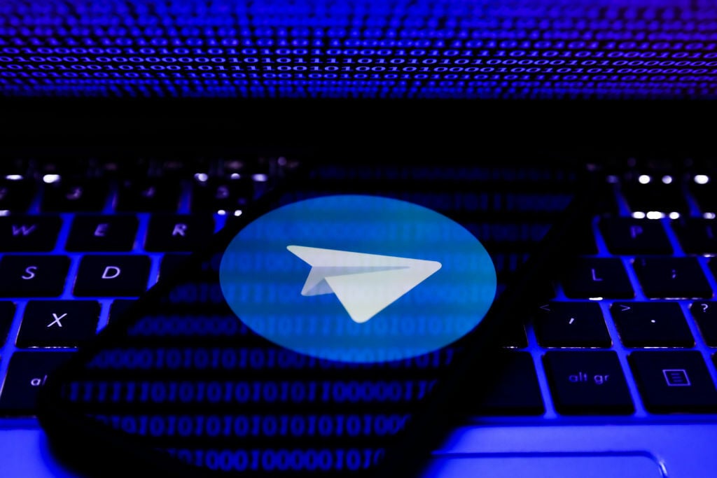 Telegram logo displayed on a phone screen and binary code displayed on a laptop screen.