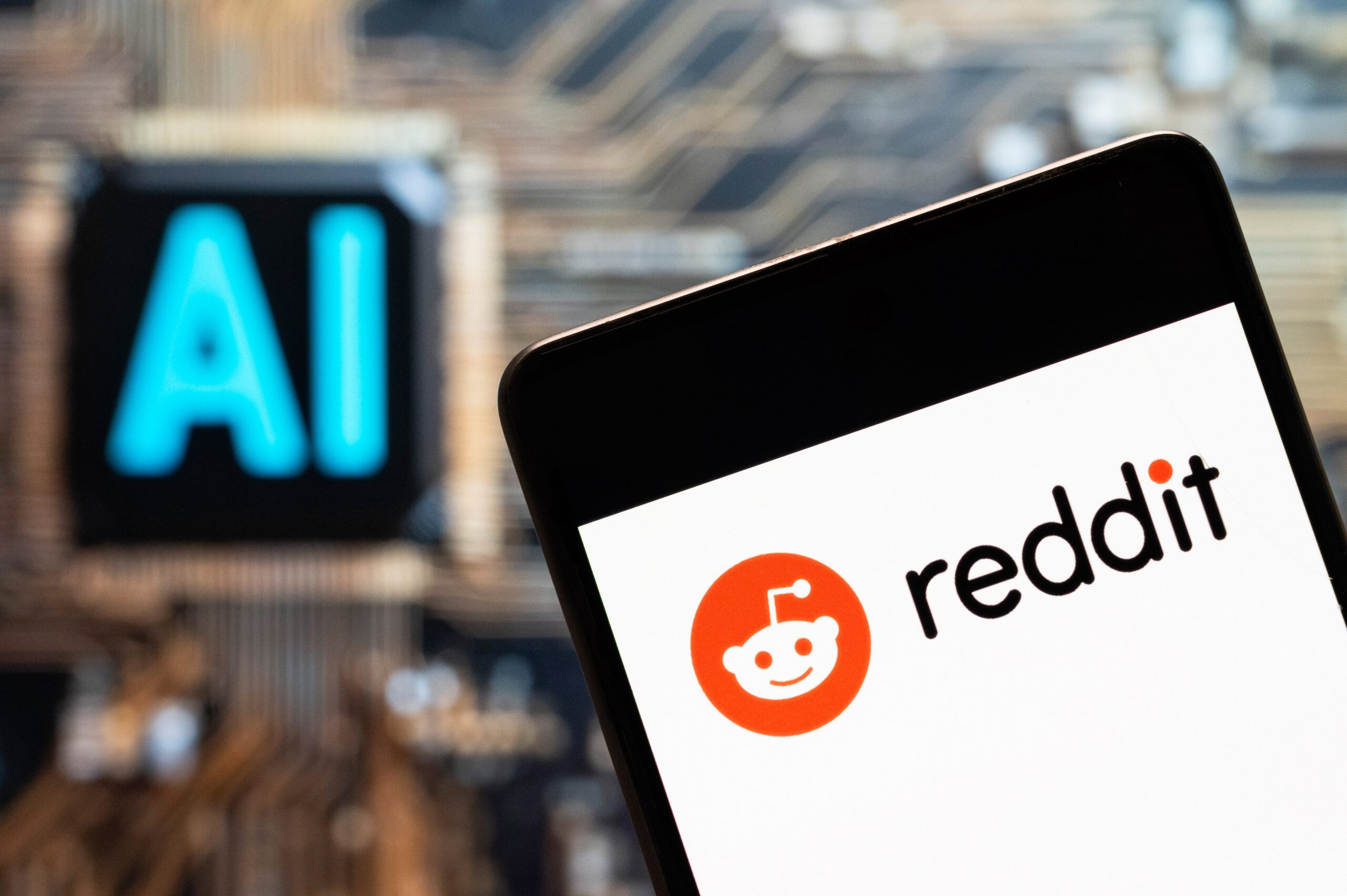A phone displaying the Reddit logo in front of a screen that reads 