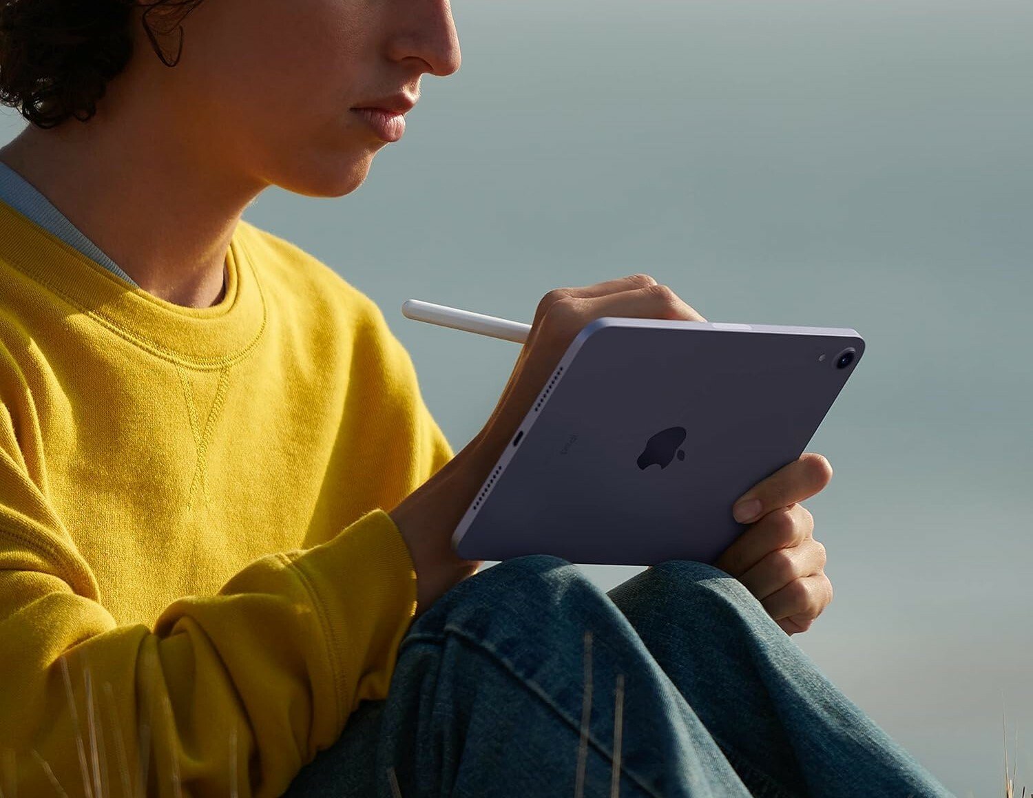 a person sits on the ground in a grassy field while writing on an ipad mini