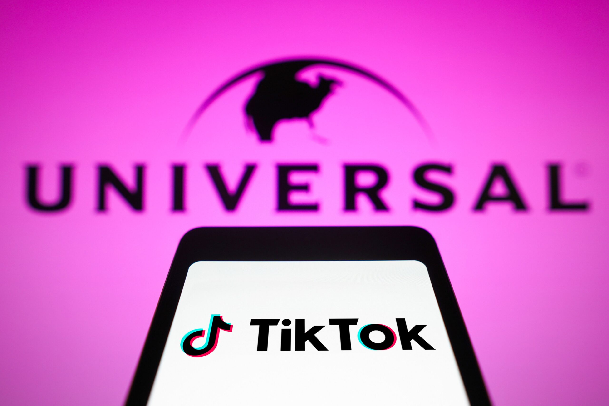 A phone displaying the TikTok logo in front of a pink sign reading 