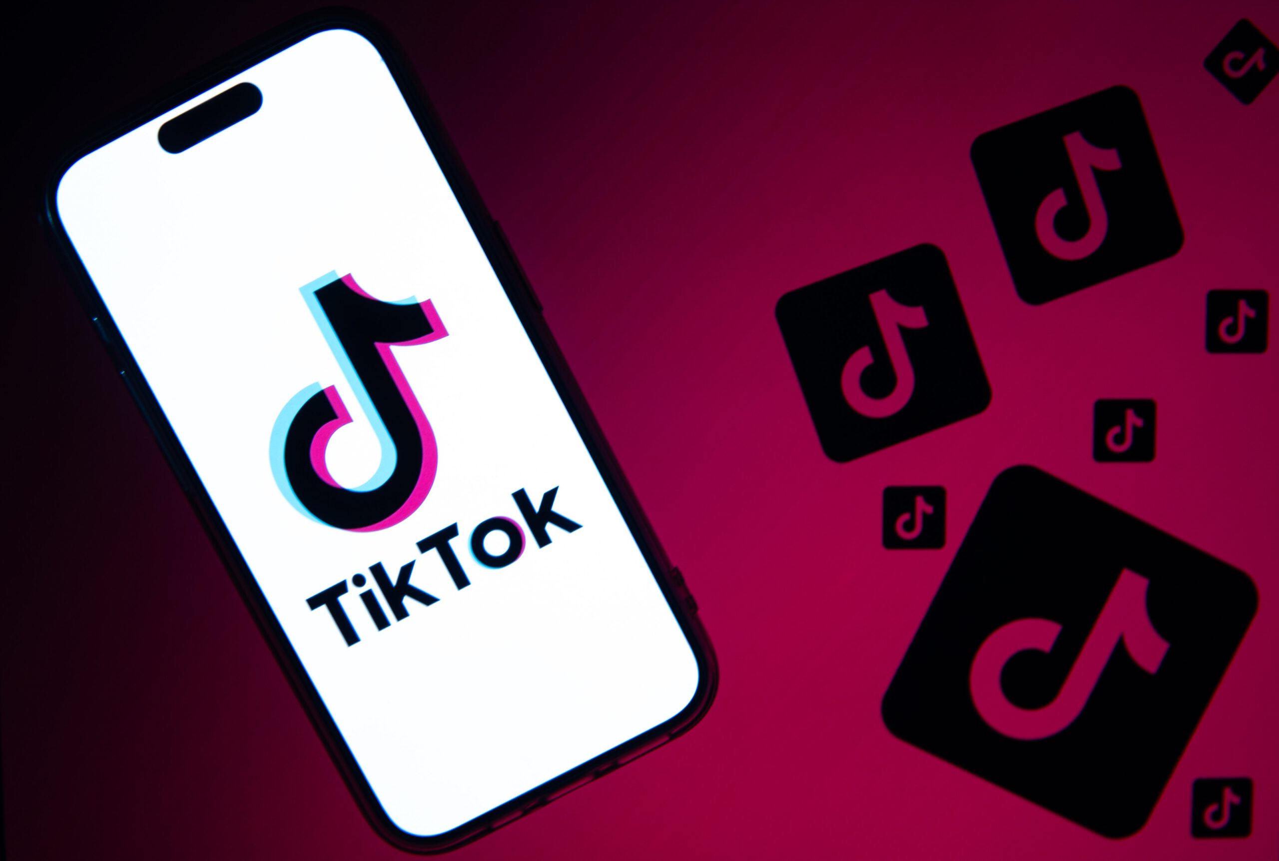 An phone screen with the TikTok logo surrounded by little TikTok logos on a pink background.