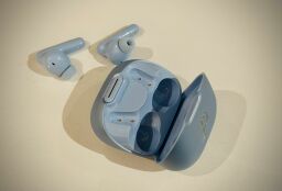 The Soundcore earbuds lying outside of their case (both in a light blue color) on a white surface