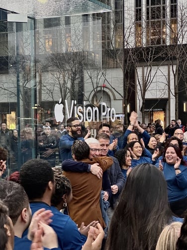Tim Cook hugs a man in a brown jacket in front of the Apple store.