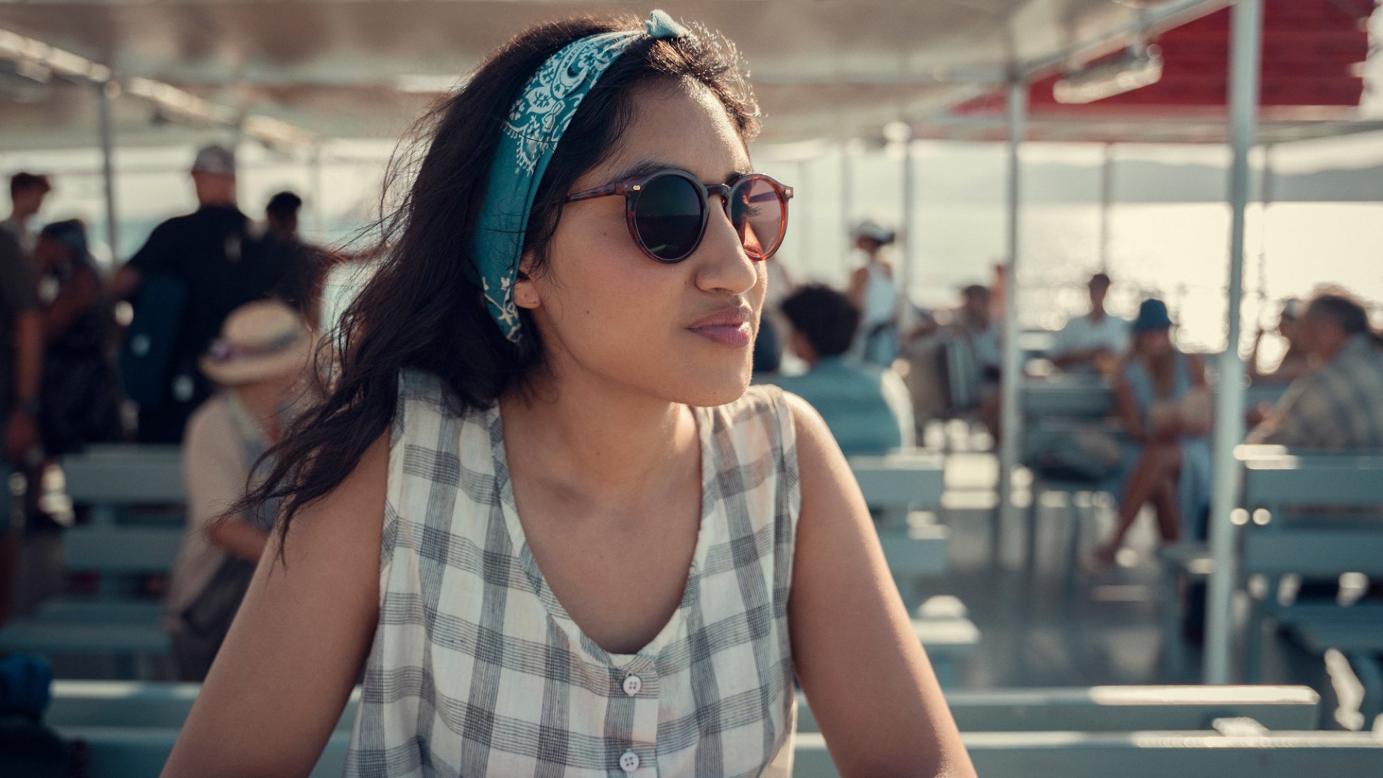 A young woman wearing sunglasses sits in the sun on a ferry.