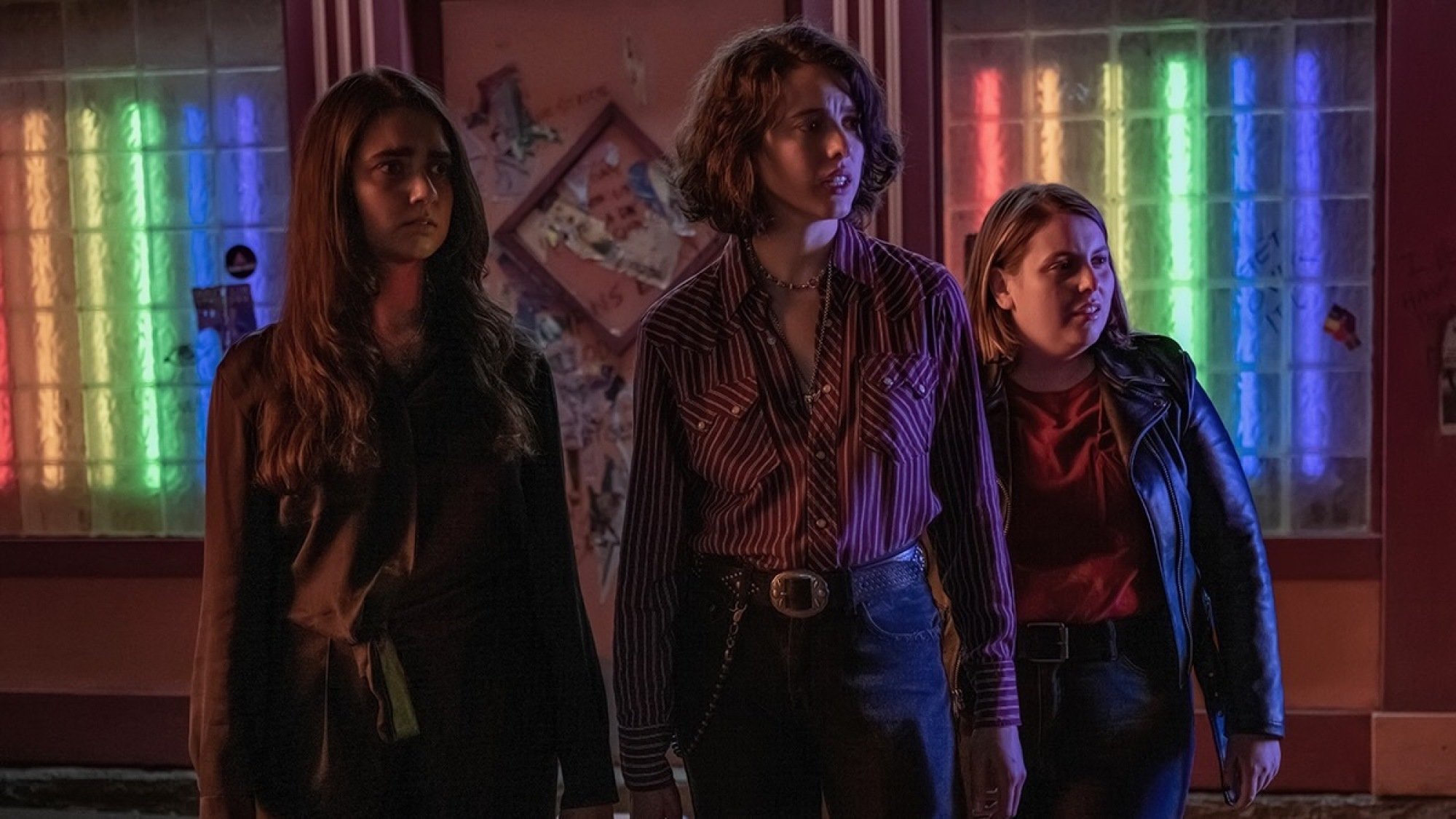 Geraldine Viswanathan, Margaret Qualley, and Beanie Feldstein stand outside a gay bar in "Drive-Away Dolls." 