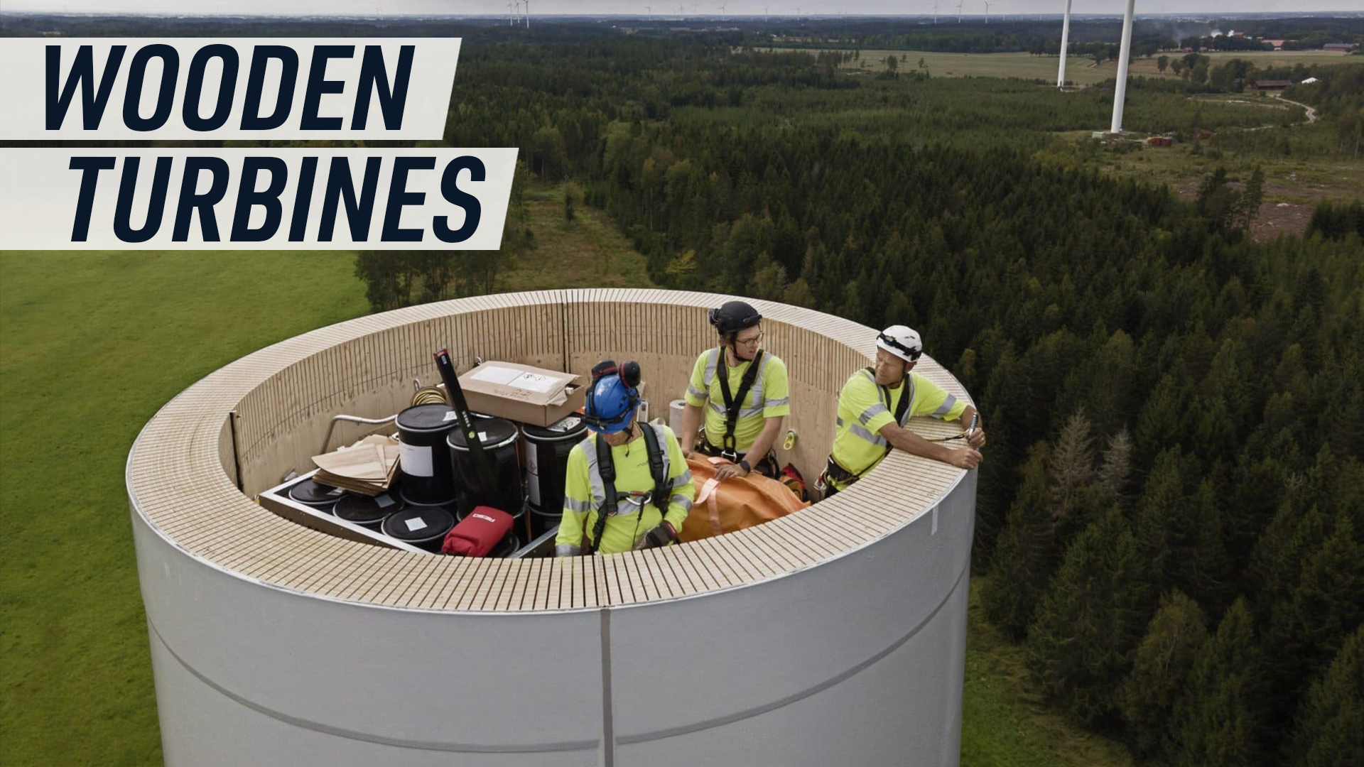 An aerial shot shows workers standing inside a wooden wind turbine as it is being constructed.