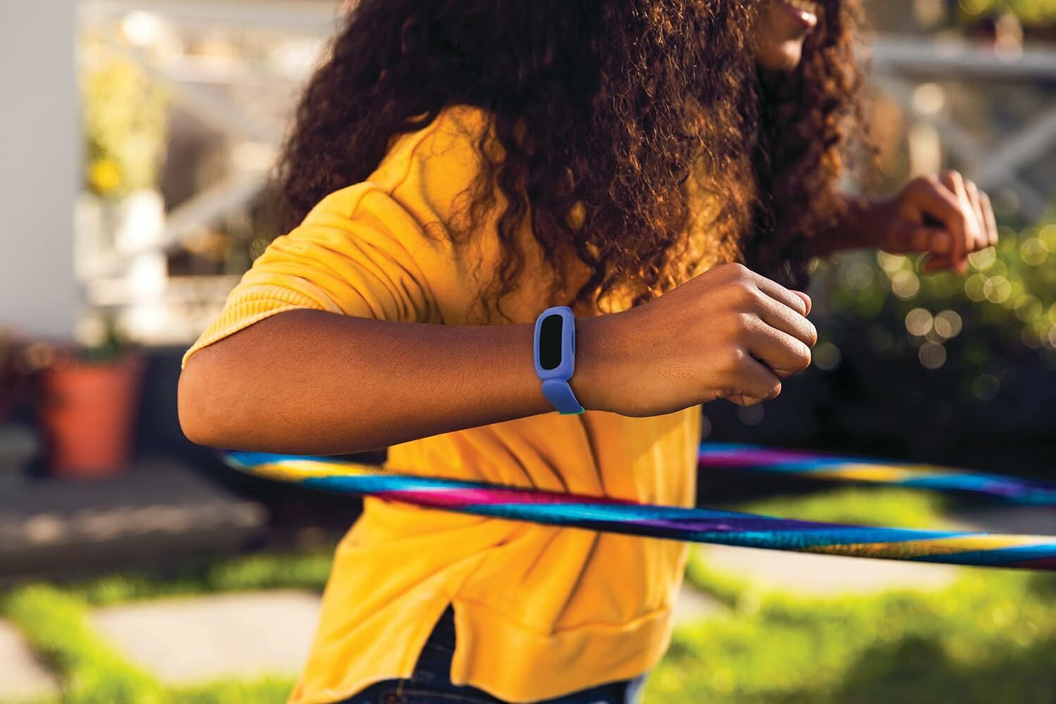 a child uses a hula hoop while wearing a blue fitbit ace 3 on the right hand
