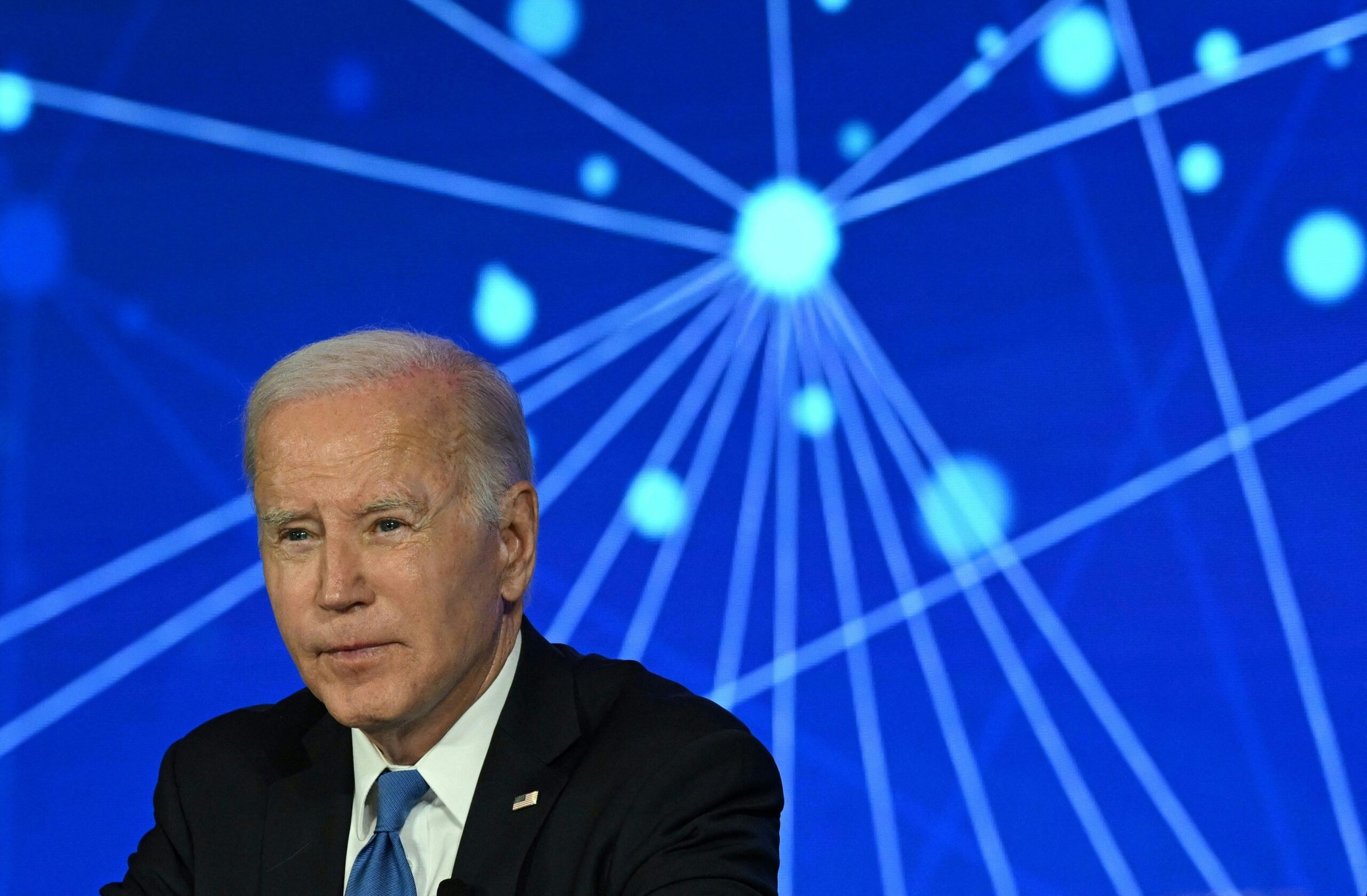 Joe Biden sits in front of an abstract blue backdrop. 